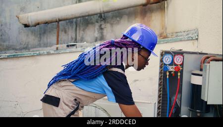 Portrait rapproché du manomètre de montage d'électricien afro-américain souriant utilisé pour vérifier le réservoir de fréon de condenseur dans le besoin de réparation. Ingénieur utilisant des manomètres à collecteur pour vérifier les niveaux de réfrigérant Banque D'Images