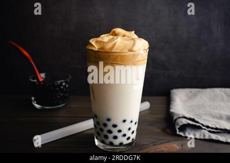 Café de Dalgona glacé avec Boba dans un verre de pinte sur un fond sombre : café de Dalgona froid avec du lait et des perles de tapioca montré avec une paille de boba Banque D'Images