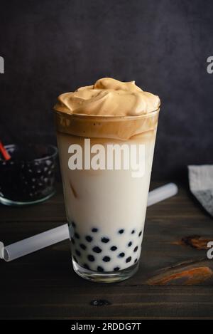 Café de Dalgona glacé avec Boba dans un verre de pinte sur un fond sombre : café de Dalgona froid avec du lait et des perles de tapioca montré avec une paille de boba Banque D'Images