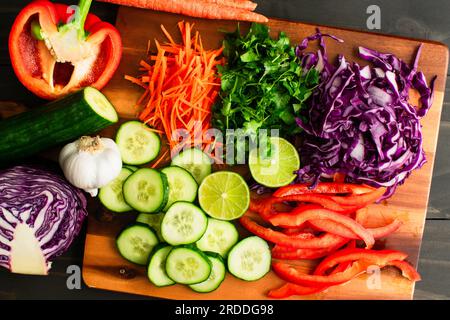 Variété de légumes frais préparés pour une salade : carottes en julienne, chou râpé avec concombre tranché, citron vert et poivron rouge Banque D'Images