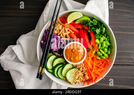 Salade de nouilles de riz avec sauce épicée aux arachides et baguettes : salade végétalienne de nouilles de riz garnie d'edamame, de carottes et d'autres légumes frais Banque D'Images