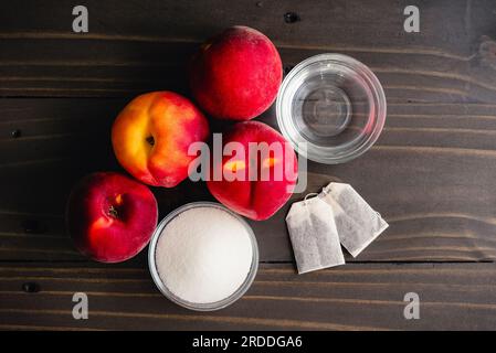 Thé glacé à la pêche vietnamienne (Trà Dào) Ingrédients sur une table en bois : pêches fraîches, sucre, sachets de thé et eau sur fond de bois sombre Banque D'Images