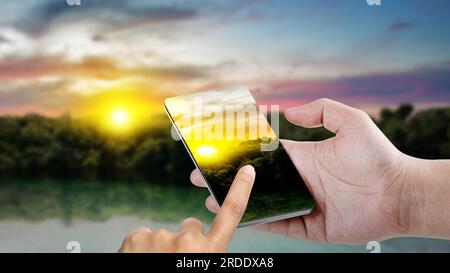 Homme prenant une photo avec son téléphone portable avec un fond de scène de coucher de soleil. Journée mondiale de la photographie Banque D'Images