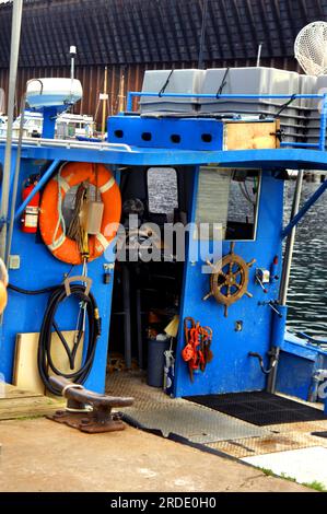 Un petit bateau de pêche est amarré au port de Marquette, Michigan. La peinture bleu vif couvre la cabine et le pont. Vieille roue nautique vintage pend assid Banque D'Images