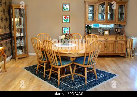 La salle à manger de style champêtre est dotée d'une table ovale en chêne et de six chaises. Les murs de l'armoire Curio et de l'armoire en porcelaine sont ornés d'un tapis à motifs et de planchers en bois. Banque D'Images