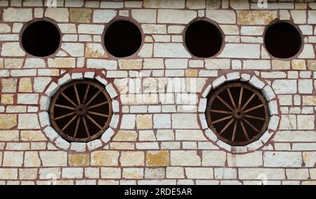 Mur de pierre rustique avec roues de wagon et portails ronds à l'intérieur. Image de fond de décoration sur le thème occidental. Banque D'Images