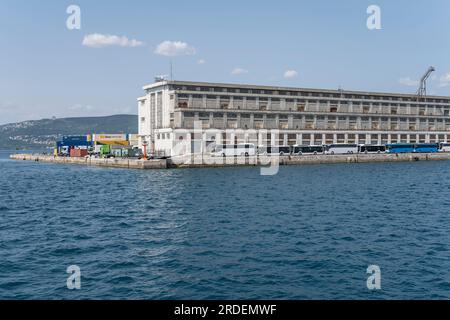 TRIESTE, ITALIE - mai 29 2023 : paysage urbain avec des bâtiments portuaires et des autocars bordés sur le quai, tourné de la mer dans une lumière vive le 29 mai 2023 à Trieste, FR Banque D'Images