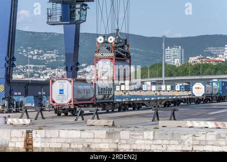 TRIESTE, ITALIE - mai 29 2023 : train et grosses grues manipulant des conteneurs sur quai, filmés de la mer dans une lumière vive le 29 mai 2023 à Trieste, Frioul, Ital Banque D'Images