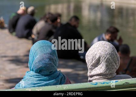 Deux femmes avec le foulard sont assises sur un banc, les hommes à l'arrière par le vieux canal, Paris, France Banque D'Images