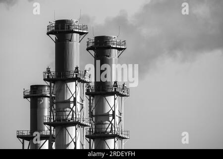 Les cheminées fumantes sont sous le ciel gris un jour. Équipement d'échappement de centrale électrique, photo noir et blanc Banque D'Images