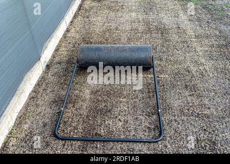Rouler les graines d'herbe fraîchement semées avec un rouleau métallique rempli d'eau. Banque D'Images