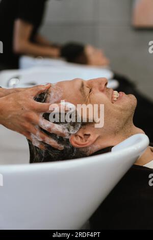 Hairstylist washing hair to handsome man in beauty salon. Banque D'Images