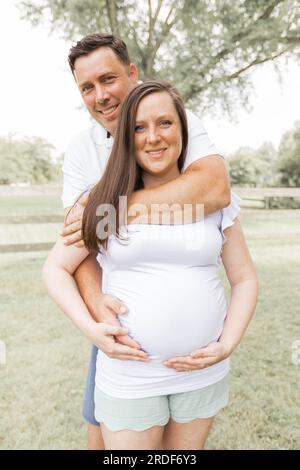Couple souriant en blanc avec les mains sur le ventre enceinte Banque D'Images