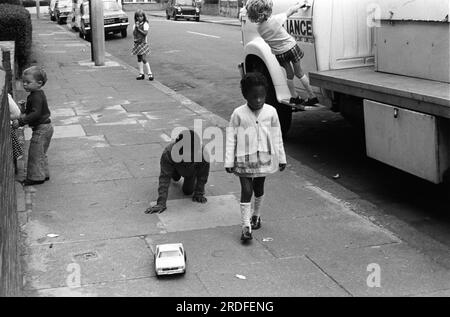 Enfants jouant dans la rue 1970s Royaume-Uni. Enfants devant leur maison familiale avec une grande voiture top. Un groupe ethnique diversifié d'enfants heureux et sûrs. Elephant and Castle, Londres, Angleterre vers 1975. Royaume-Uni HOMER SYKES Banque D'Images