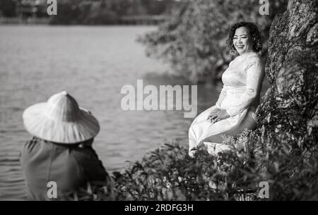 Une femme vietnamienne d'âge moyen portant un « Ao Dai » traditionnel pose pour une photographie à côté du lac Hoan Kiem dans le centre de Hanoi, au Vietnam. Banque D'Images