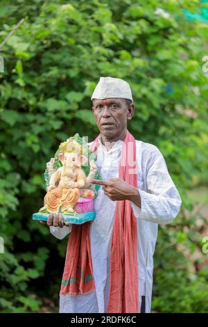 Vieil homme indien tenant l'idole du Seigneur Ganesha dans les mains, heureux vieux pauvre homme Banque D'Images