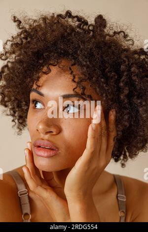 Belle dame avec la coiffure curly posant contre le mur beige Banque D'Images