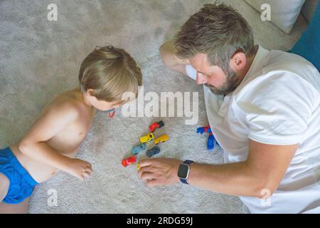 Temps de jeu. Joyeux père aimant jouer des voitures colorées avec son petit fils, passer du temps libre ensemble à l'intérieur de la maison Banque D'Images