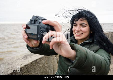 Jeune femme vénézuélienne latine voyageur sur la jetée à côté de la rivière à Buenos Aires, souriant très heureux de prendre une photo selfie avec un DSRL numérique est venu Banque D'Images