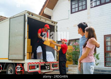 Un couple asiatique se tient ensemble, observant avec anticipation alors que les travailleurs emménagent dans leur nouvelle maison. L'excitation remplit l'air alors qu'ils anticipent avec impatience Banque D'Images