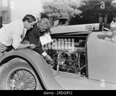 Hollywood, Californie : c. 1922 l'acteur john Bowers reçoit quelques conseils sur son moteur Duesenberg du pilote de voiture de course Ralph de Palma. Bowers participera aux courses annuelles du jour de Thanksgiving de Los Angeles. Banque D'Images