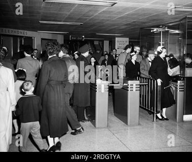 Toronto, Canada : c. 1957 Une scène dans la station de métro Queen Street avec des passagers qui traversent des tourniquets. Banque D'Images