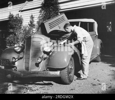 Connecticutt : 1936 Un homme travaillant sur sa voiture devant son garage. Banque D'Images