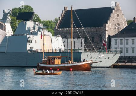 Autour de Bergen - Un bateau à rames étant passé par un bateau de pêche local, avec F361 HDMS Iver Huitfeldt en arrière-plan Banque D'Images