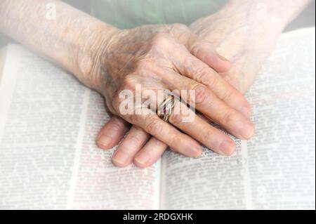 Les vieilles mains s'attachent ensemble au-dessus d'une Bible ouverte. Les mains sont froissées et portées avec les soucis du monde. Banque D'Images