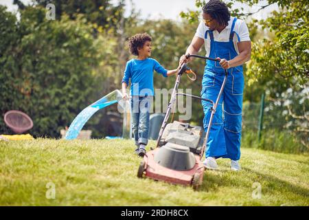 Père et fils dehors dans la cour tondre l'herbe avec tondeuse à gazon, fils aidant son père dans le jardinage. Famille afro-américaine. Banque D'Images