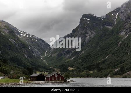 Maison norvégienne rouge traditionnelle debout seule dans le fjord. Village isolé dans la nature sauvage. Paysage scandinave Moody. Banque D'Images