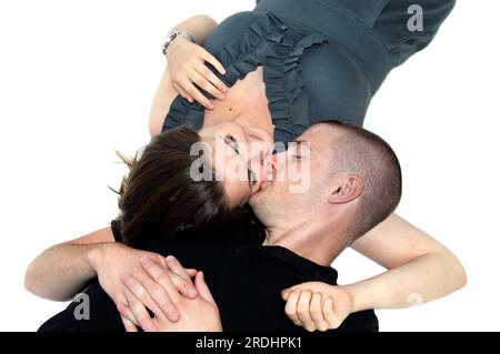 Jeune homme et jeune femme étaient couchés sur tout le sol blanc près l'un de l'autre. L'homme l'embrasse sur la joue et elle sourit. Il porte une chemise noire et Banque D'Images