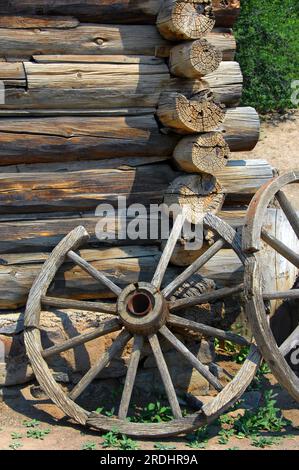 Deux roues de wagon rustiques s'appuient contre un mur de cabane en rondins sur le sentier historique national El Rancho de Las Golondrinas. Banque D'Images