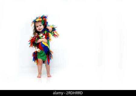 Adorable petite fille porte un costume d'oiseau à plumes et tient un petit oiseau en peluche. Elle est debout dans un espace tout blanc avec de la place pour le design et pe Banque D'Images