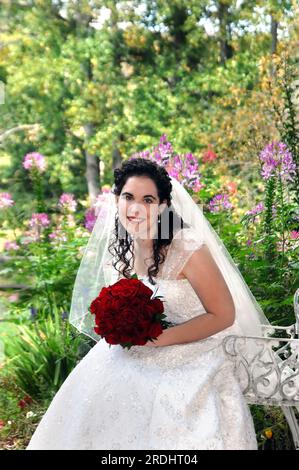 Beau pont est entouré de fleurs et jardin. Elle tient un bouquet de roses rouges et sourit joyeusement. Banque D'Images