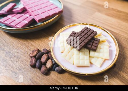 Assiettes avec barres chocolatées faites à la main. Concept de bonbons haut de gamme. Ruby chocolat noir et blanc et fèves de chocolat disposées sur une table en bois. Photo de haute qualité Banque D'Images