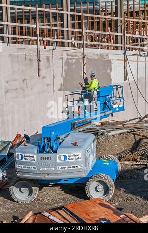 Travailleur dans le panier d'un élévateur ou d'un piqueur de cerises travaillant sur le côté d'une structure sur un chantier de construction. Banque D'Images