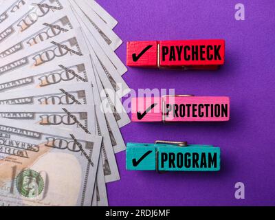 Billets de banque avec le mot PROGRAMME DE PROTECTION DE CHÈQUE DE PAIE sur fond violet Banque D'Images