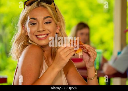 Une magnifique jeune mannequin blonde profite de son déjeuner à l’extérieur tout en maintenant une distance sécuritaire des autres pendant la pandémie de Covid-19 Banque D'Images