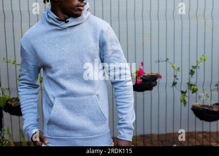 Section médiane de l'homme afro-américain portant un sweat-shirt à capuche gris contre la clôture blanche, espace copie Banque D'Images