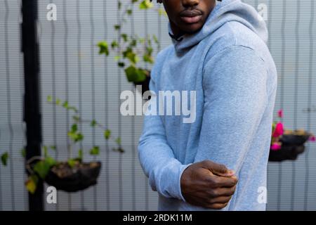 Section médiane de l'homme afro-américain portant un sweat-shirt à capuche gris contre la clôture blanche, espace copie Banque D'Images