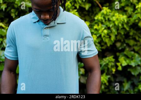 Section médiane de l'homme afro-américain portant un polo bleu pâle dans le jardin Banque D'Images