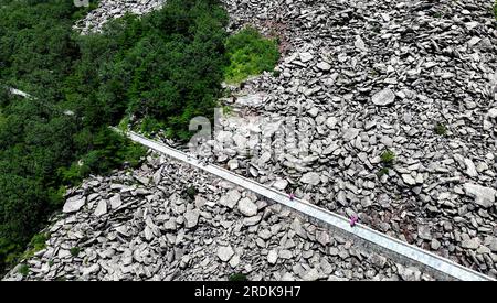 Xi'an. 21 juillet 2023. Cette photo aérienne prise le 21 juillet 2023 montre des visiteurs passant devant la mer rocheuse dans le parc forestier national de Zhuque à Xi'an, dans la province du Shaanxi, au nord-ouest de la Chine. Le parc, situé dans le cours supérieur de la rivière Laohe est et dans le nord des montagnes Qinling, couvre une superficie de 2 621 hectares, et son point culminant Bingjing pic a une altitude de 3 015 mètres. Des paysages étonnants tels que la forêt vierge, les restes de glaciers et la mer de nuages peuvent être vus le long de la route vers le sommet. Crédit : Liu Xiao/Xinhua/Alamy Live News Banque D'Images