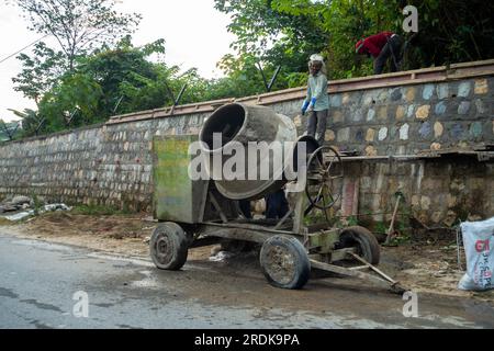 28 juin 2023, Uttarakhand, Inde. Construction du mur de soutènement en pierre le long de la route latérale avec la machine de mélange et les ouvriers sur le site. Banque D'Images