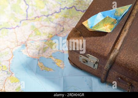 Bateau en papier plié sur une vieille valise vintage placée sur une carte, voyage, wanderlust et concept de croisière, espace de copie, mise au point sélectionnée, profondeur de champ étroite Banque D'Images