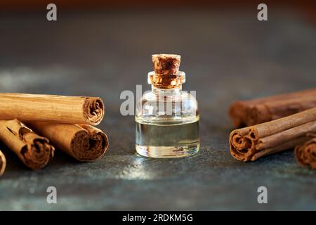 Une bouteille d'huile essentielle d'aromathérapie avec de vrais bâtons de cannelle sur fond sombre Banque D'Images