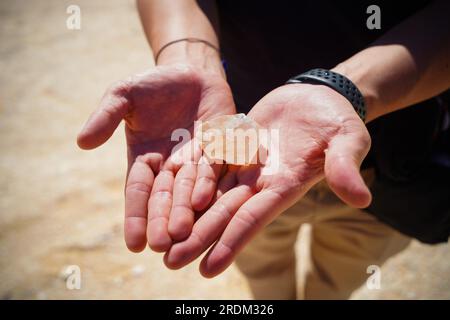 Un touriste vu montrant un morceau de quartz trouvé sur le sol près de la «montagne de cristal» dans le désert blanc, Egypte. De l'érosion des volcans et d'une montagne de quartz, aux roches altérées et aux formations rocheuses de craie blanche, Black and White Desert fait partie de la dépression de Frarafra dans le désert du Sahara et se situe dans la partie occidentale de l'Égypte. Le vaste désert est relié aux routes principales qui sont proches de la frontière libyo-égyptienne où il est maintenant lourdement armé avec une présence militaire. Le paysage naturel bizarre s'élevant d'un fond océanique il y a des millions d'années est maintenant laissé avec des formations karstiques calcaires qui re Banque D'Images