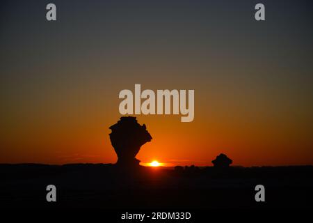 Soleil vu se coucher dans le désert blanc, Egypte. De l'érosion des volcans et d'une montagne de quartz, aux roches altérées et aux formations rocheuses de craie blanche, Black and White Desert fait partie de la dépression de Frarafra dans le désert du Sahara et se situe dans la partie occidentale de l'Égypte. Le vaste désert est relié aux routes principales qui sont proches de la frontière libyo-égyptienne où il est maintenant lourdement armé avec une présence militaire. Le paysage naturel bizarre qui s'élève d'un fond océanique il y a des millions d'années est maintenant laissé avec des formations karstiques calcaires qui ressemblent à la surface d'autres planètes de l'univers. (Photo de Banque D'Images