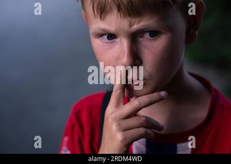 Portrait d'un garçon se cueillant le nez. Un garçon réfléchi sillonne ses sourcils. Banque D'Images