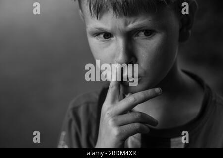 Portrait d'un garçon se cueillant le nez. Un garçon réfléchi sillonne ses sourcils. Image en noir et blanc. Banque D'Images